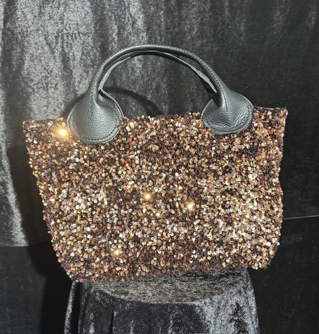 Bronzefarbene Paillettentasche mit schwarzen Griffen, kunstvoll beleuchtet.